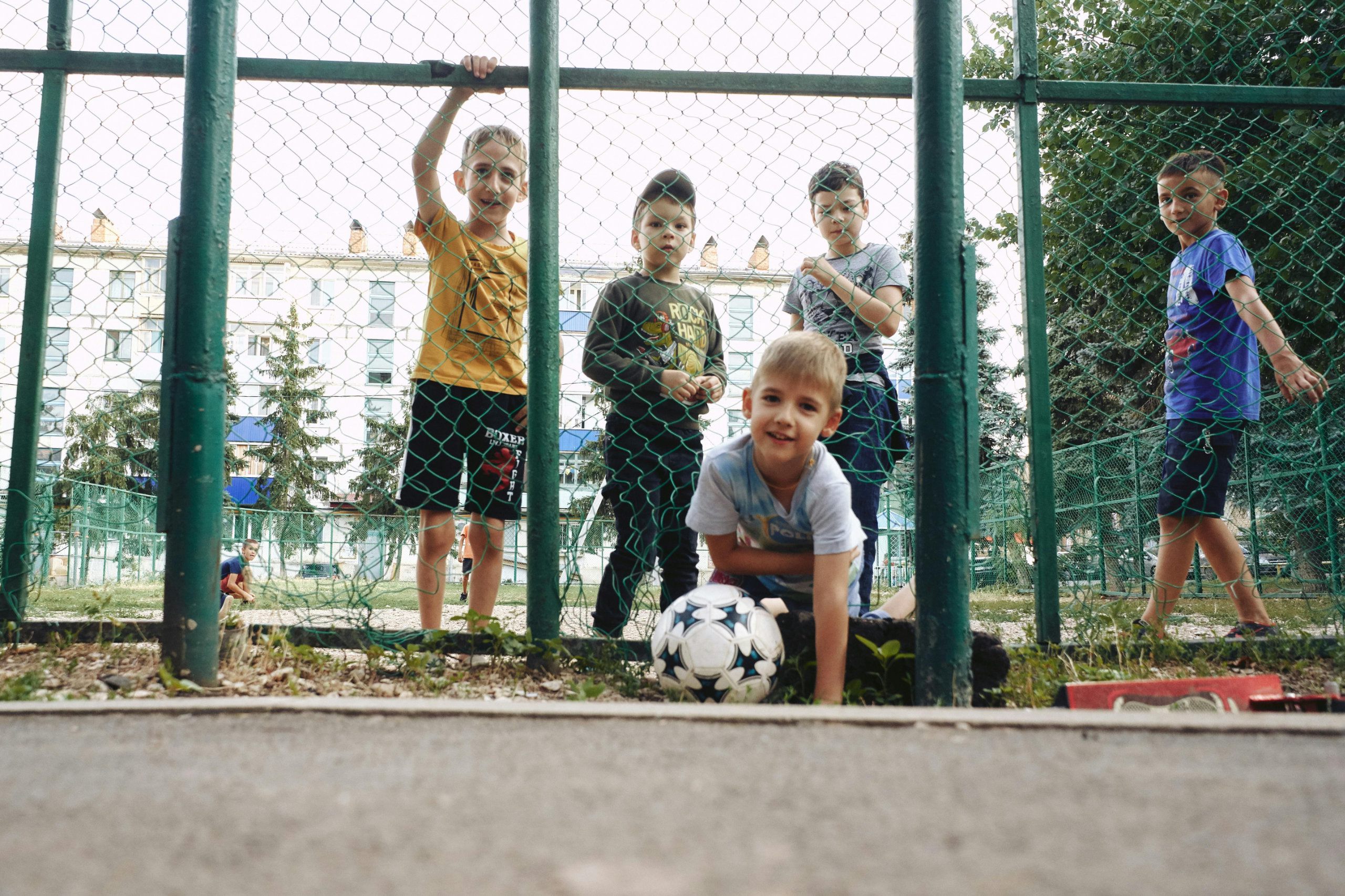 % Jungs auf einem Sportplatz hinter dem Zaun vor ihnen ein Fußball